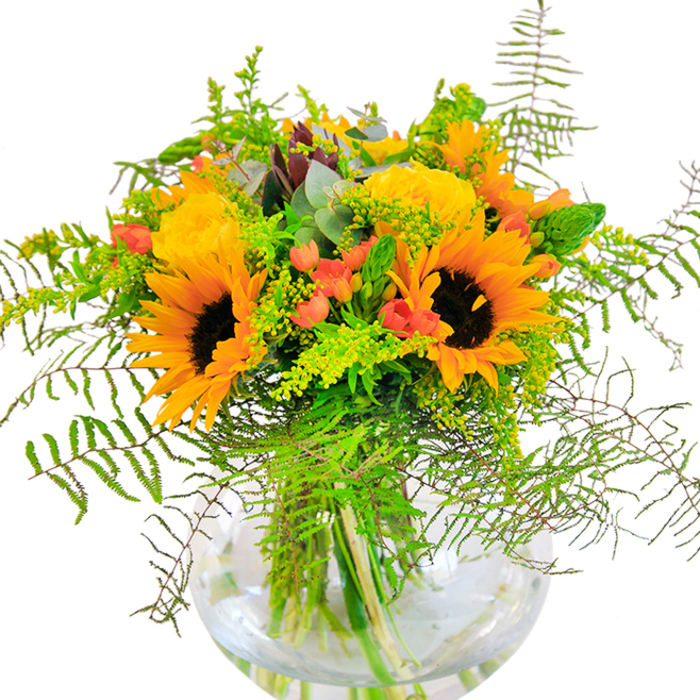 There's an air of cultivated joy in this Belgravia-inspired bouquet, as if gathered after a peaceful morning among the garden squares and botanical walkways of the neighbourhood. Sunflowers, vivid and statuesque, take centre stage-their golden petals bright against deep, earthy centres, calling to mind sunlit corners of Elizabeth Street or quiet stoops along Chesham Place. Tucked amongst these are tufts of yellow filler flowers, likely solidago, each one a pinpoint of sunshine adding depth and movement to the composition. Pops of coral-orange blooms inject a playful flourish, their cup shapes peeking from layered greenery. Soft, arching fern fronds and blue-tinged eucalyptus leaves introduce both classical charm and crisp modernity, like an artful border around a Chelsea Flower Show exhibit. The arrangement basks in the natural clarity provided by the spherical glass vase, where fresh-cut stems and pristine water are as much a part of the design as the blossoms themselves. Whether marking a milestone occasion or bringing daily cheer to a Pimlico townhouse, this bouquet expresses the refined creativity found in every corner of Belgravia, making it both a delight for the senses and a celebration of local artistry.